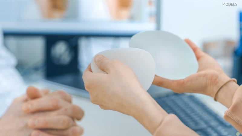 Woman holding two different breast implants during a consultation with her surgeon.