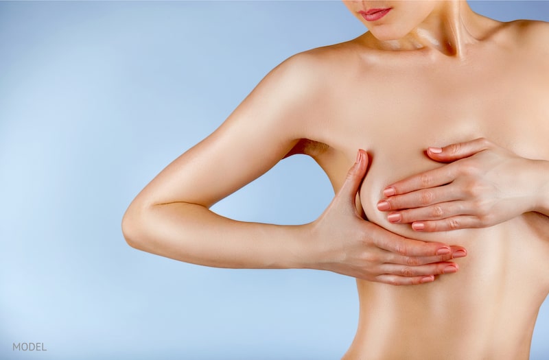 Woman pressing against her breast against a blue background.